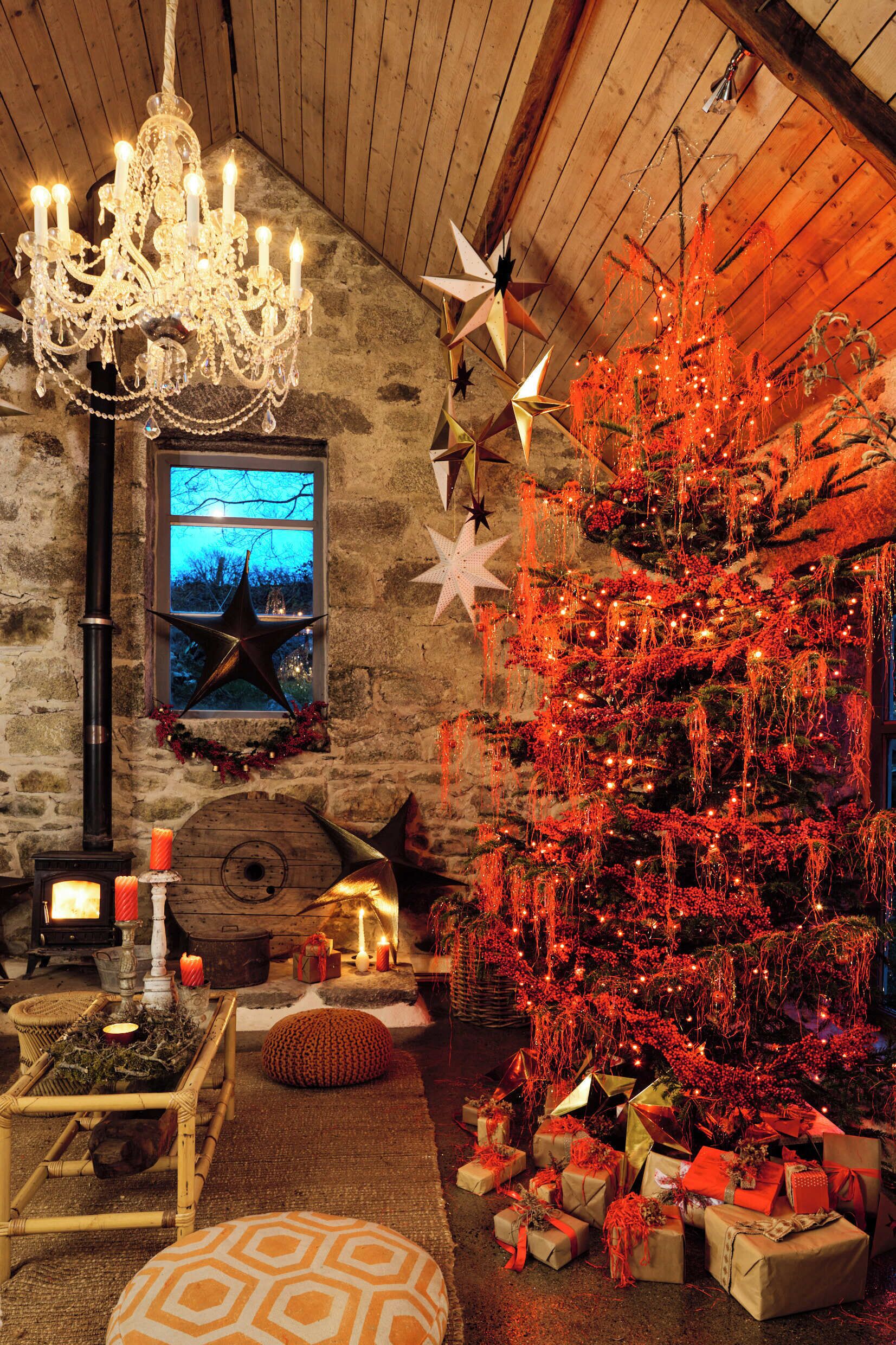 A rustic room with a large Christmas tree, a chandelier, and a star decoration on the wall.