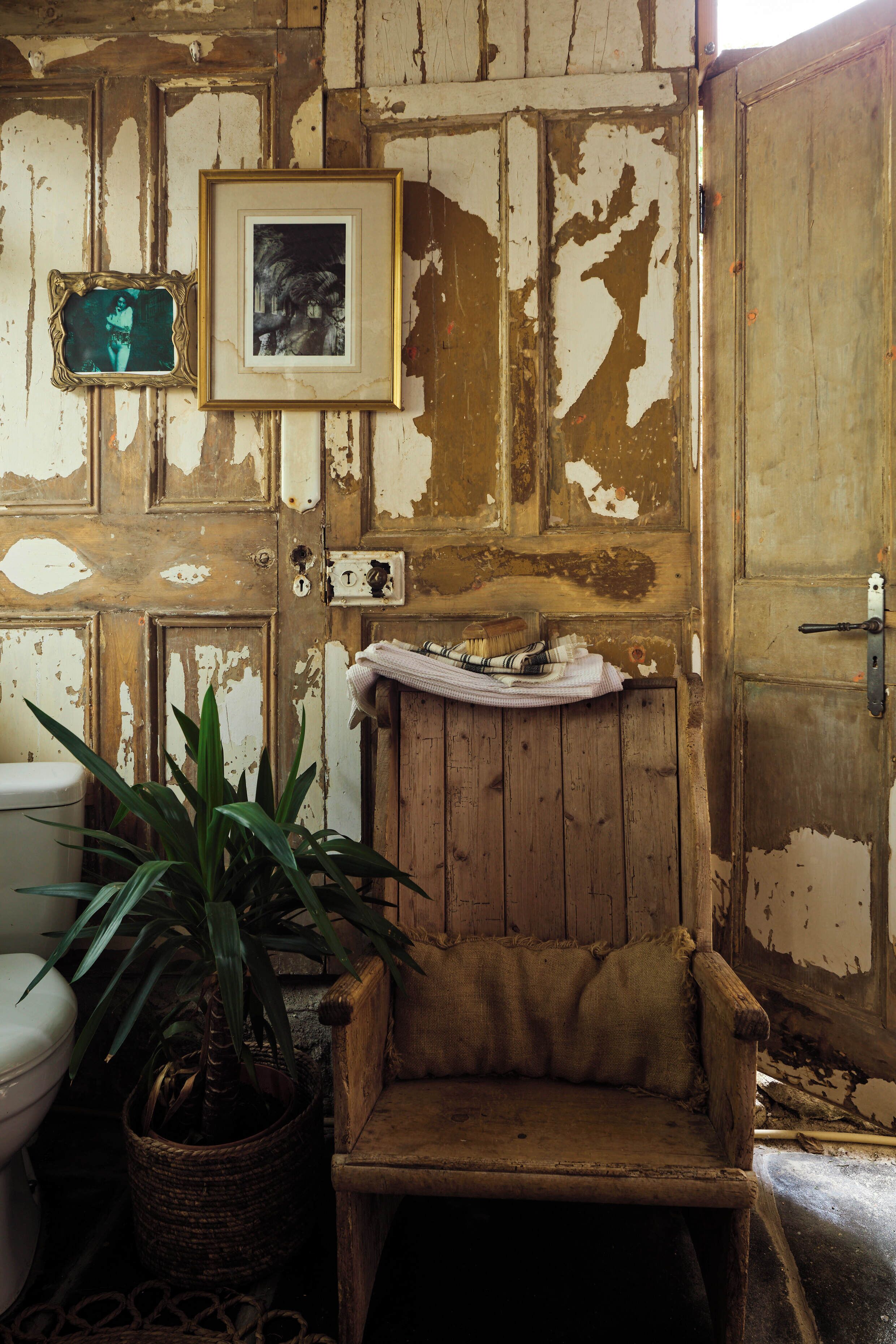 Un baño rústico con una puerta de madera, un cuadro enmarcado, una planta en maceta y una toalla en el suelo.