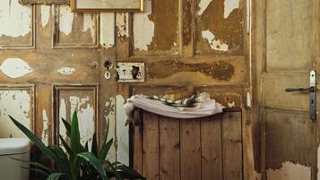 Un baño rústico con una puerta de madera, un cuadro enmarcado, una planta en maceta y una toalla en el suelo.
