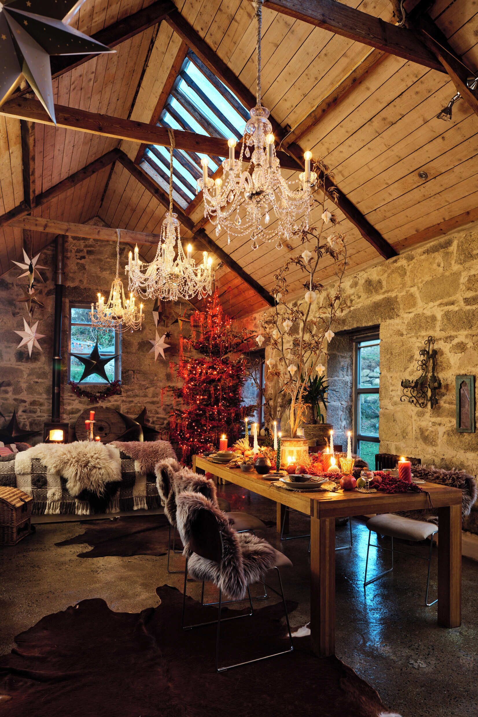 Ein rustikales Interieur mit Holzbalkendecke, Steinwänden, einer Chandelüster, einem Weihnachtsbaum und einem festlich gedeckten Esstisch.