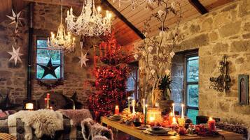 Ein rustikales Interieur mit Holzbalkendecke, Steinwänden, einer Chandelüster, einem Weihnachtsbaum und einem festlich gedeckten Esstisch.