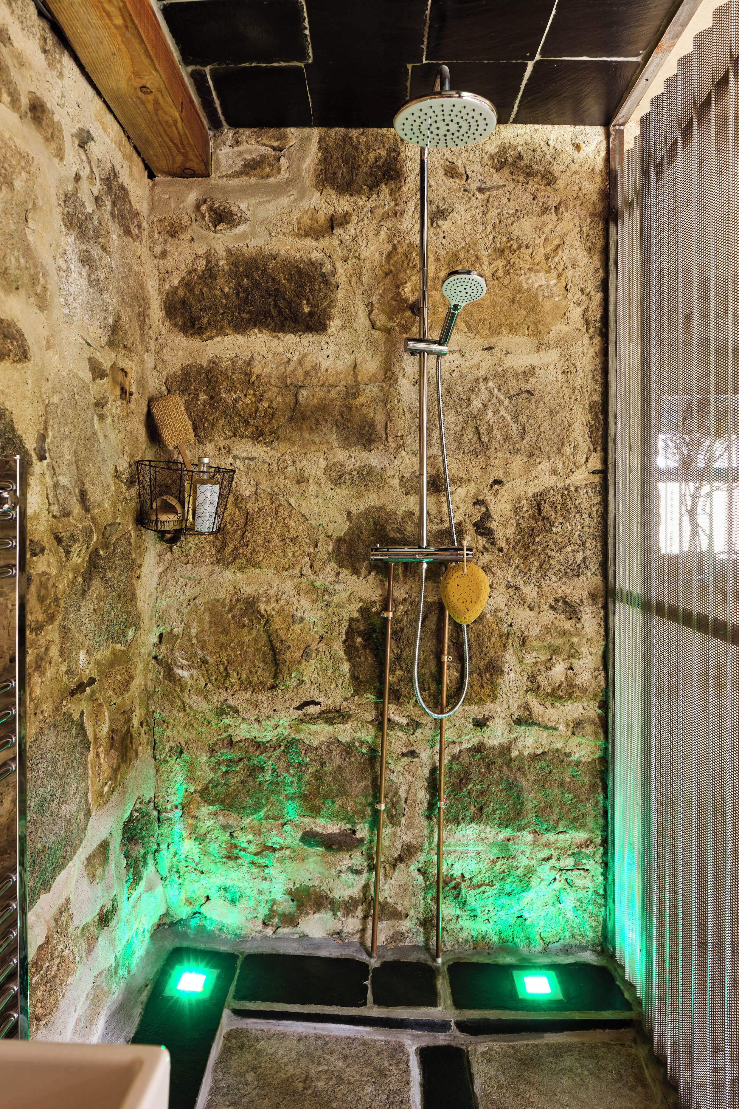 A stone-walled shower with a handheld showerhead, a wall-mounted soap dish, and a green-lit floor.