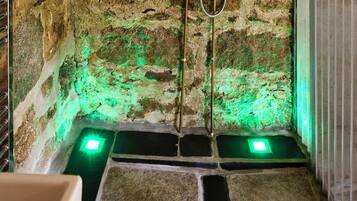 A stone-walled shower with a handheld showerhead, a wall-mounted soap dish, and a green-lit floor.