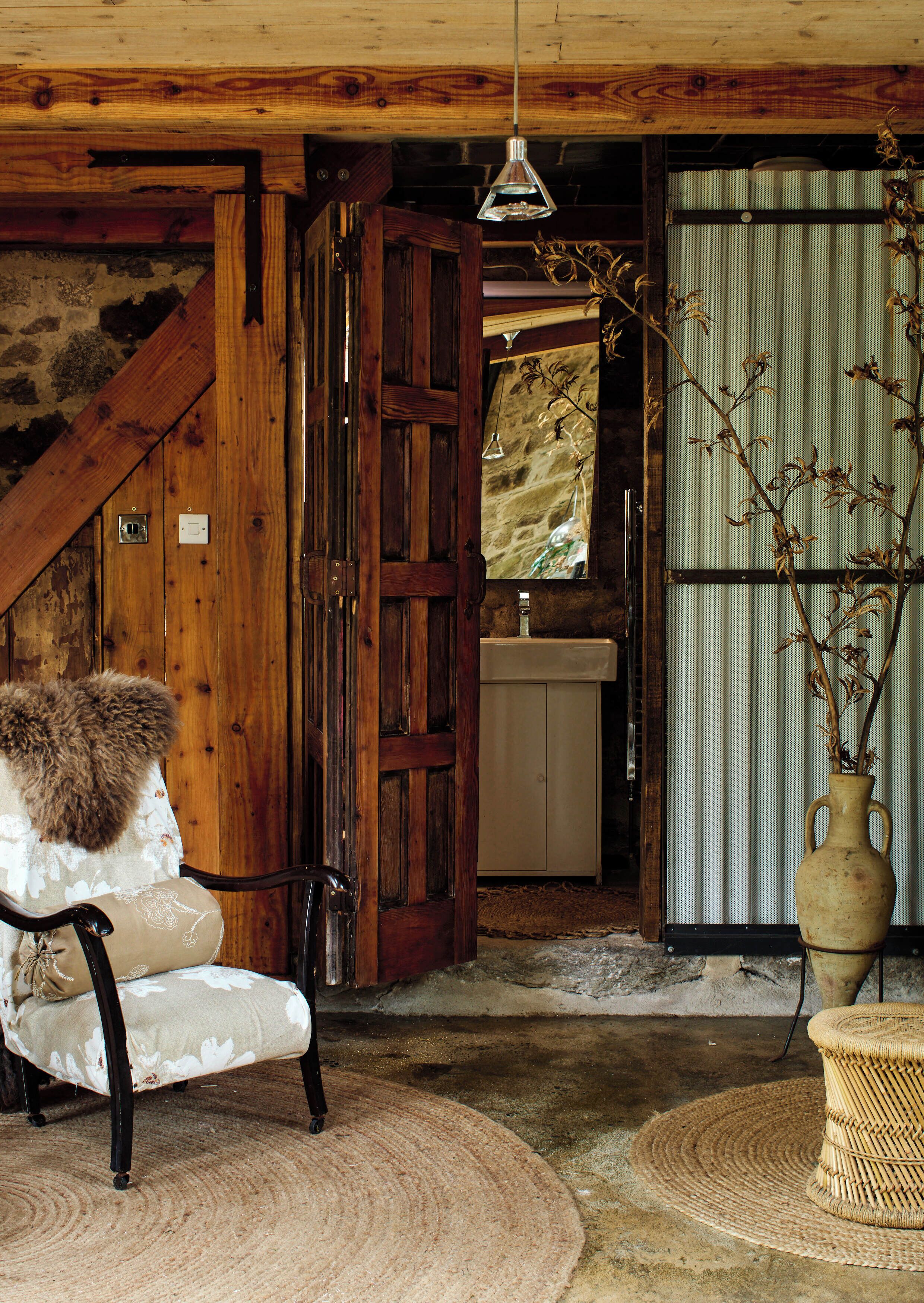 A rustic room with a wooden chair, a vase with dried branches, and a hanging light fixture.