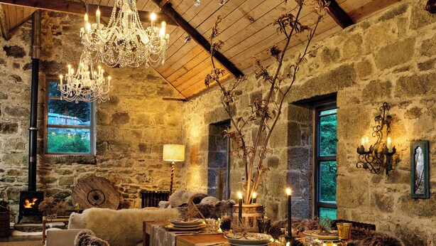 A rustic interior with stone walls, wooden beams, a chandelier, a fireplace, and a cozy seating area. - Crab Lane Studios (Shillelagh)
