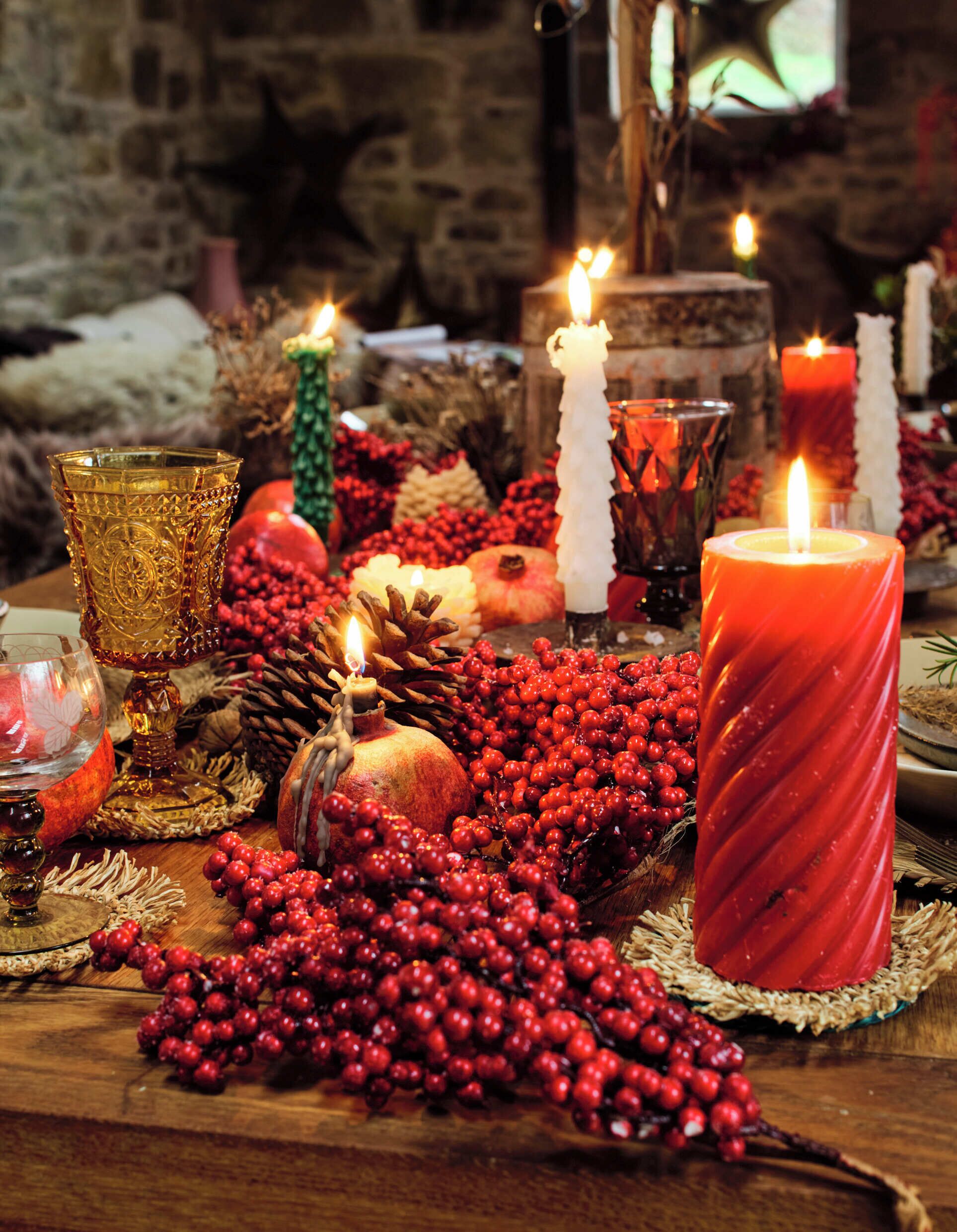 Une table décorée de bougies, d’une grenade et de baies rouges, évoquant une ambiance festive ou de fêtes.