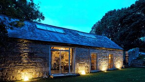 A stone building with large glass doors and windows, a sloped roof, and a well-lit exterior at dusk. - Crab Lane Studios (Shillelagh)