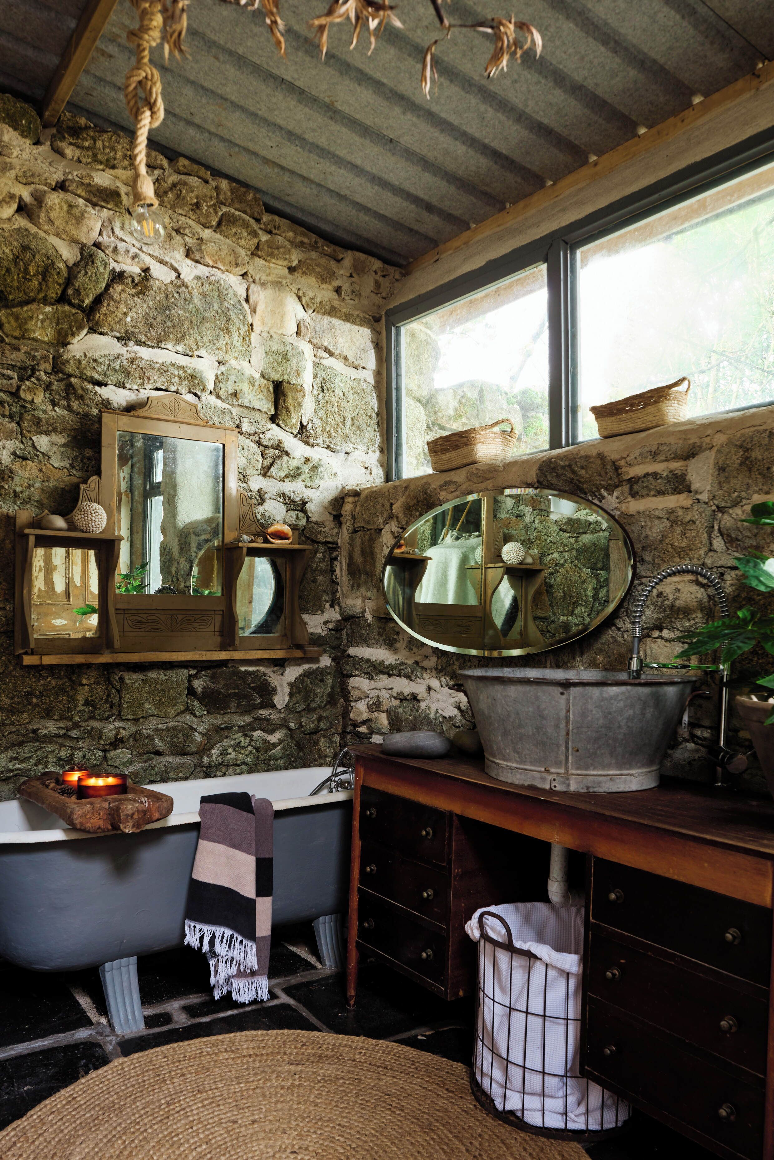 A rustic bathroom with a stone wall, a bathtub, a wooden vanity, and a large mirror.