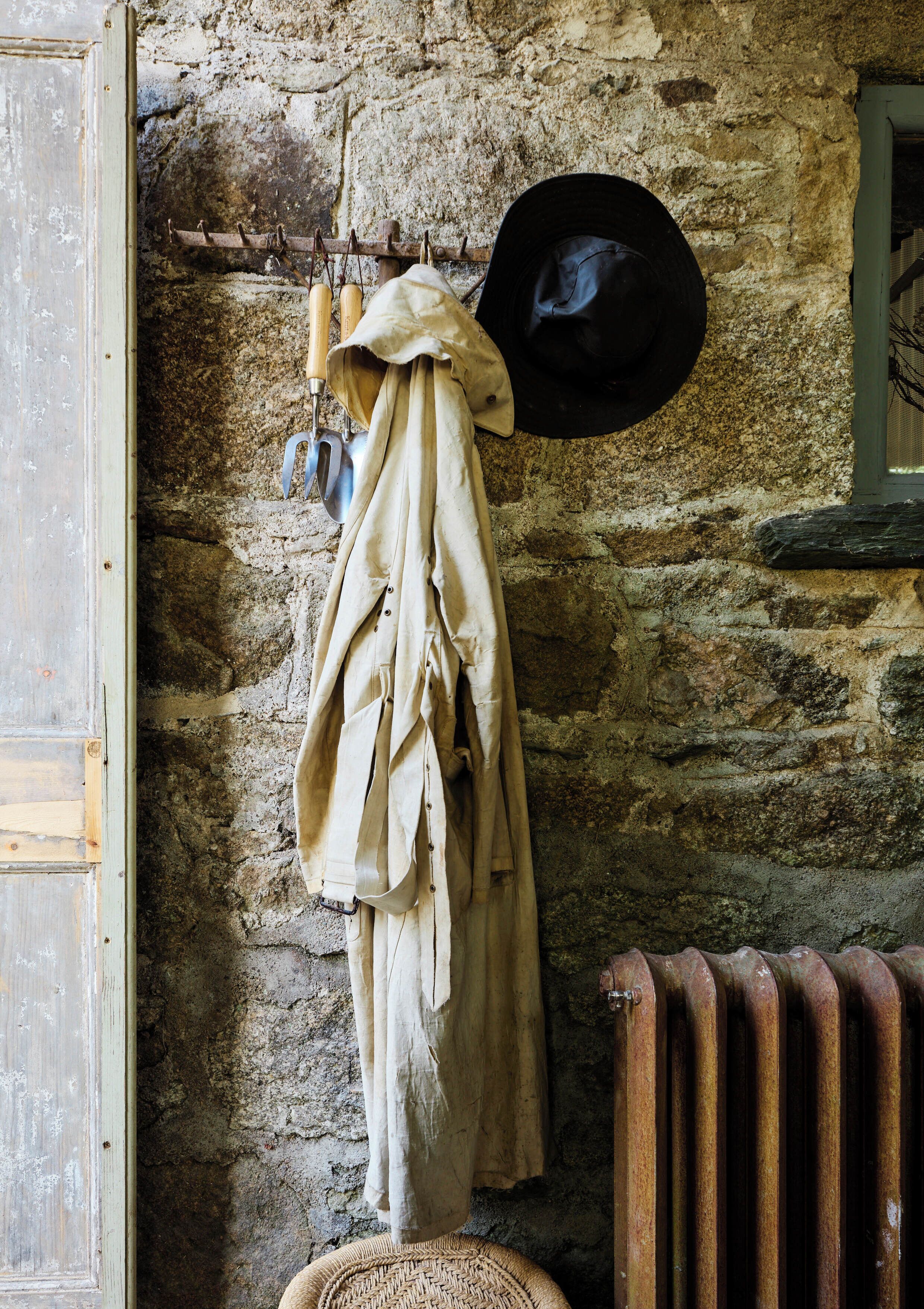 A rustic room with a stone wall, a coat hanging on a rack, a hat, and a radiator.