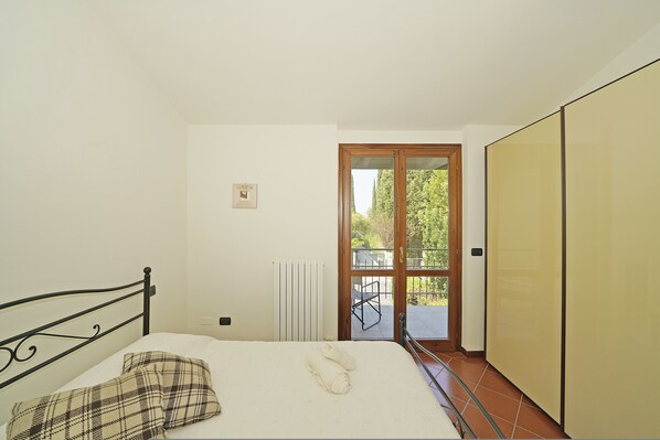 A bedroom with a bed, a radiator, a window, and a door leading to an outdoor area.