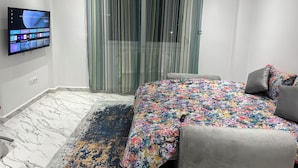 A modern bedroom with a large bed, a television mounted on the wall, and a window with sheer curtains. - Luxury apartment f4 with terrace on 2 floors in a private residence El Achour (El Achour)