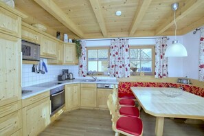 A kitchen with wooden cabinets, a microwave, a stove, and a dining area with a table and chairs. - Beautiful Alpine Chalet With Sauna (Wald im Pinzgau)