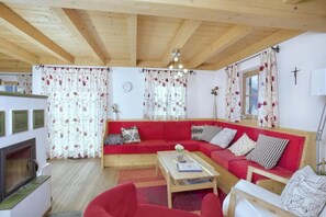 A cozy living room with a red sofa, a wooden ceiling, and a fireplace. - Beautiful Alpine Chalet With Sauna (Wald im Pinzgau)