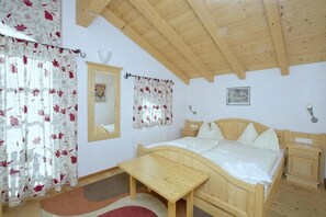 A bedroom with a wooden bed, a bedside table, a nightstand, a mirror, and a window with floral curtains. - Beautiful Alpine Chalet With Sauna (Wald im Pinzgau)