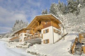 A wooden chalet with a balcony, set on a snowy slope with trees in the background. - Beautiful Alpine Chalet With Sauna (Wald im Pinzgau)