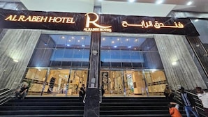 The exterior of Al Rabeh Hotel with a prominent sign, large glass windows, and a staircase leading to the entrance. - Al Rabeh Hotel (Makkah)