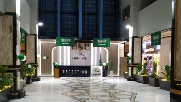 A hotel reception area with a geometric patterned floor, reception desk, and directional signs. - Al Rabeh Hotel (Makkah)