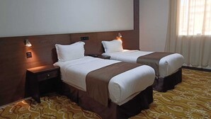 A hotel room with two beds, a nightstand, a wall-mounted light, and a patterned carpet. - Al Rabeh Hotel (Makkah)