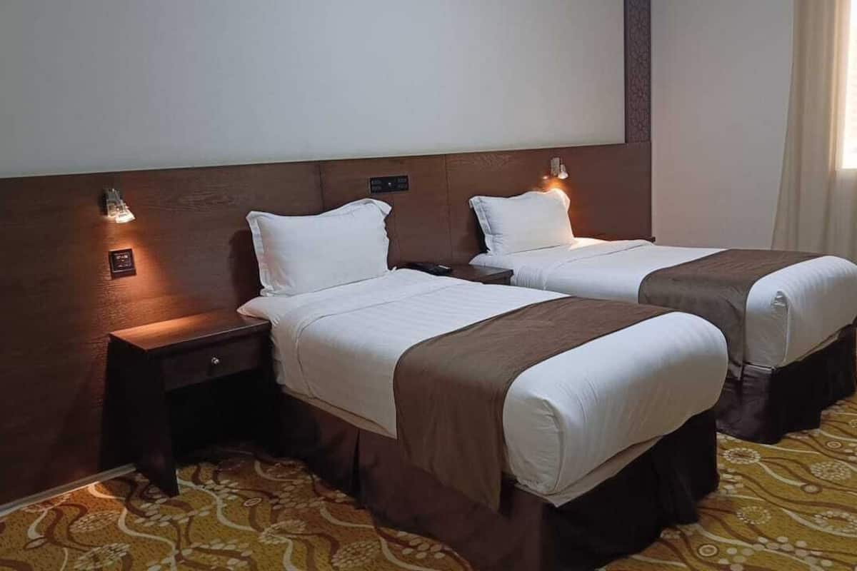 A hotel room with two beds, a nightstand, a wall-mounted light, and a patterned carpet.