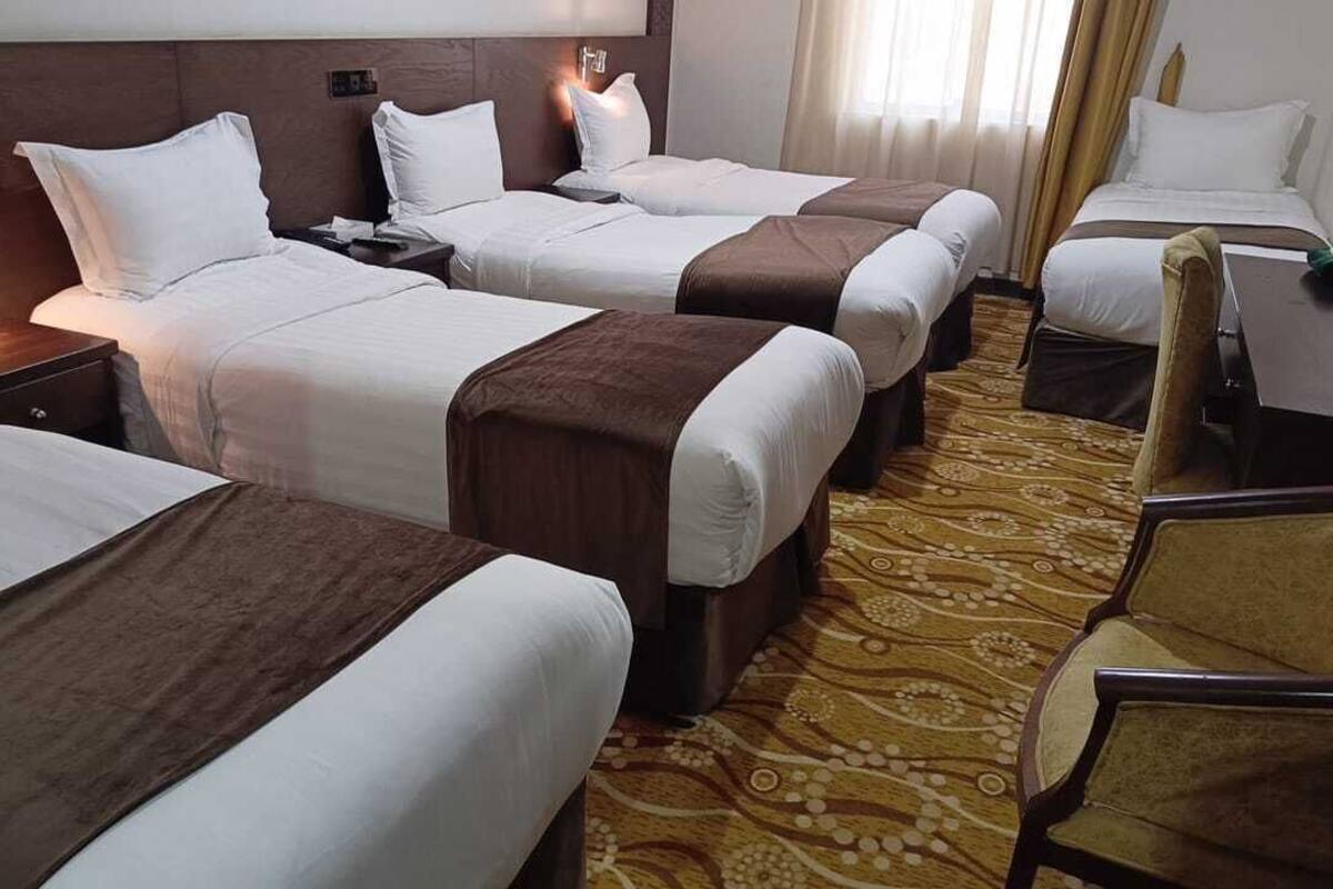 A hotel room with four beds arranged in a row, a wooden headboard, a patterned carpet, and a desk with a chair.