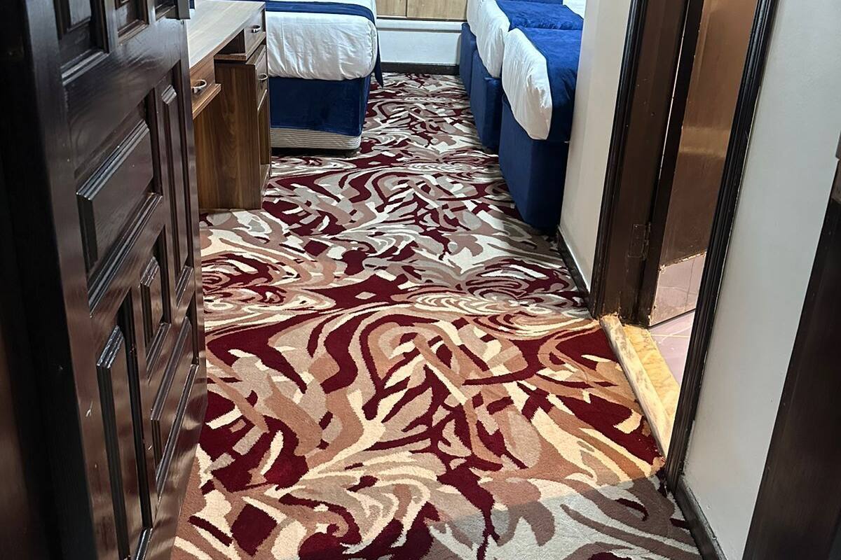 A narrow hallway with a patterned carpet leading to a bedroom with a bed and a wardrobe.