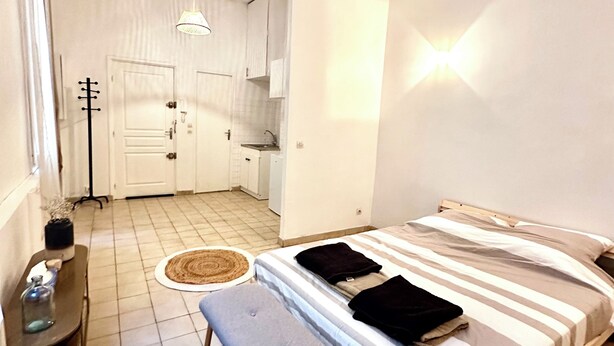 A bedroom with a bed, bench, bedside table, and a small kitchenette area. - Comfortable apartment Paris 75009 (Paris)