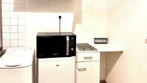 A compact kitchen with white cabinets, a microwave, a refrigerator, and a small countertop. - Comfortable apartment Paris 75009 (Paris)