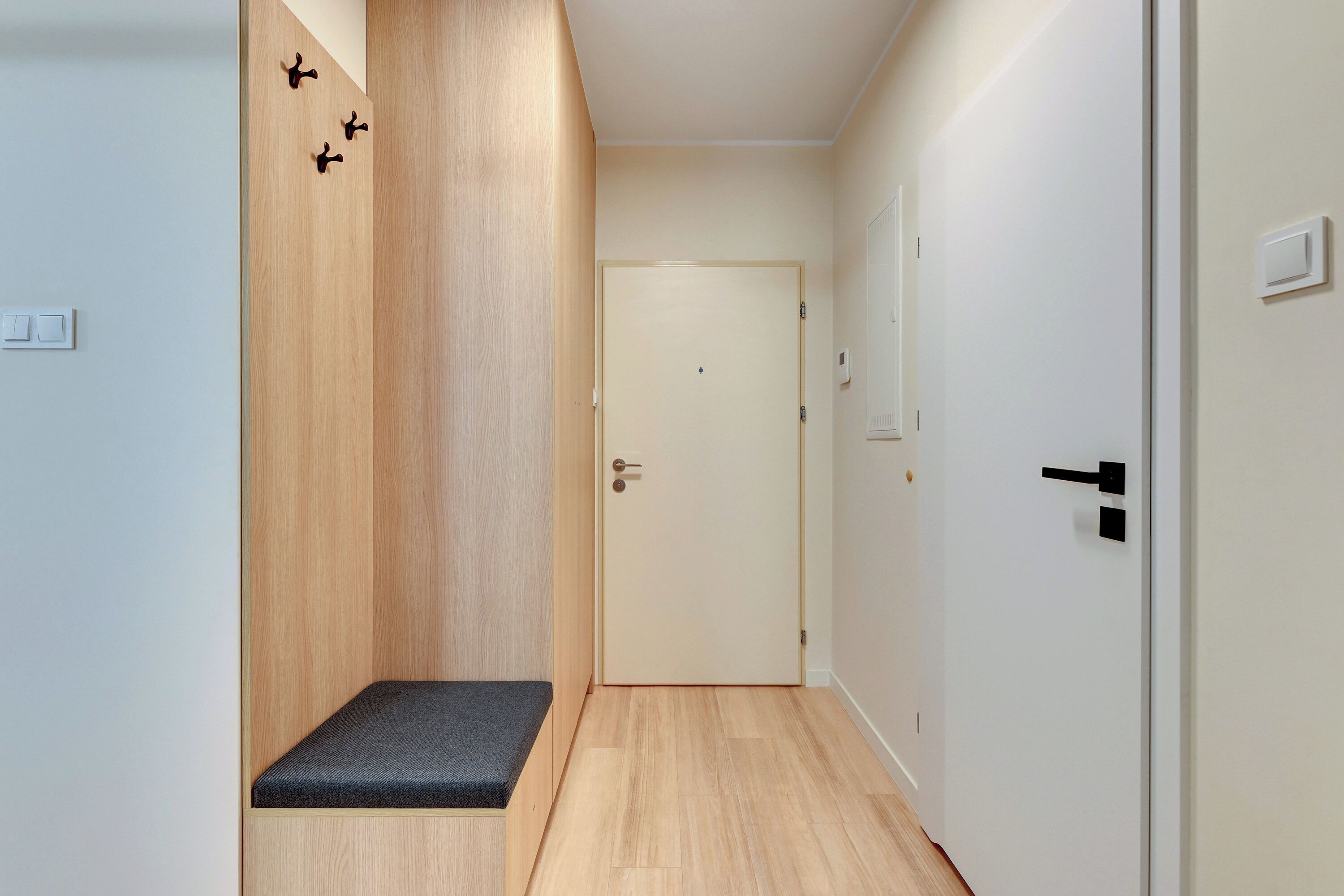 A hallway with a wooden wall, a bench, a door, and a light switch.