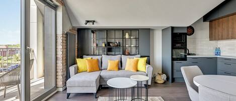 A modern living room with a grey sectional sofa, two white round tables, and a view of the city through large windows.