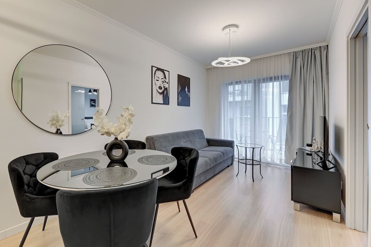 Un salon moderne avec une table de salle à manger ronde, des chaises noires à revêtement en tissu, un canapé gris et un meuble de rangement noir pour les appareils électroniques.