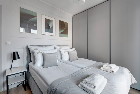 A modern bedroom with a large bed, white bedding, and a nightstand with a lamp. - Grano Residence by Downtown Apartments (Gdansk)