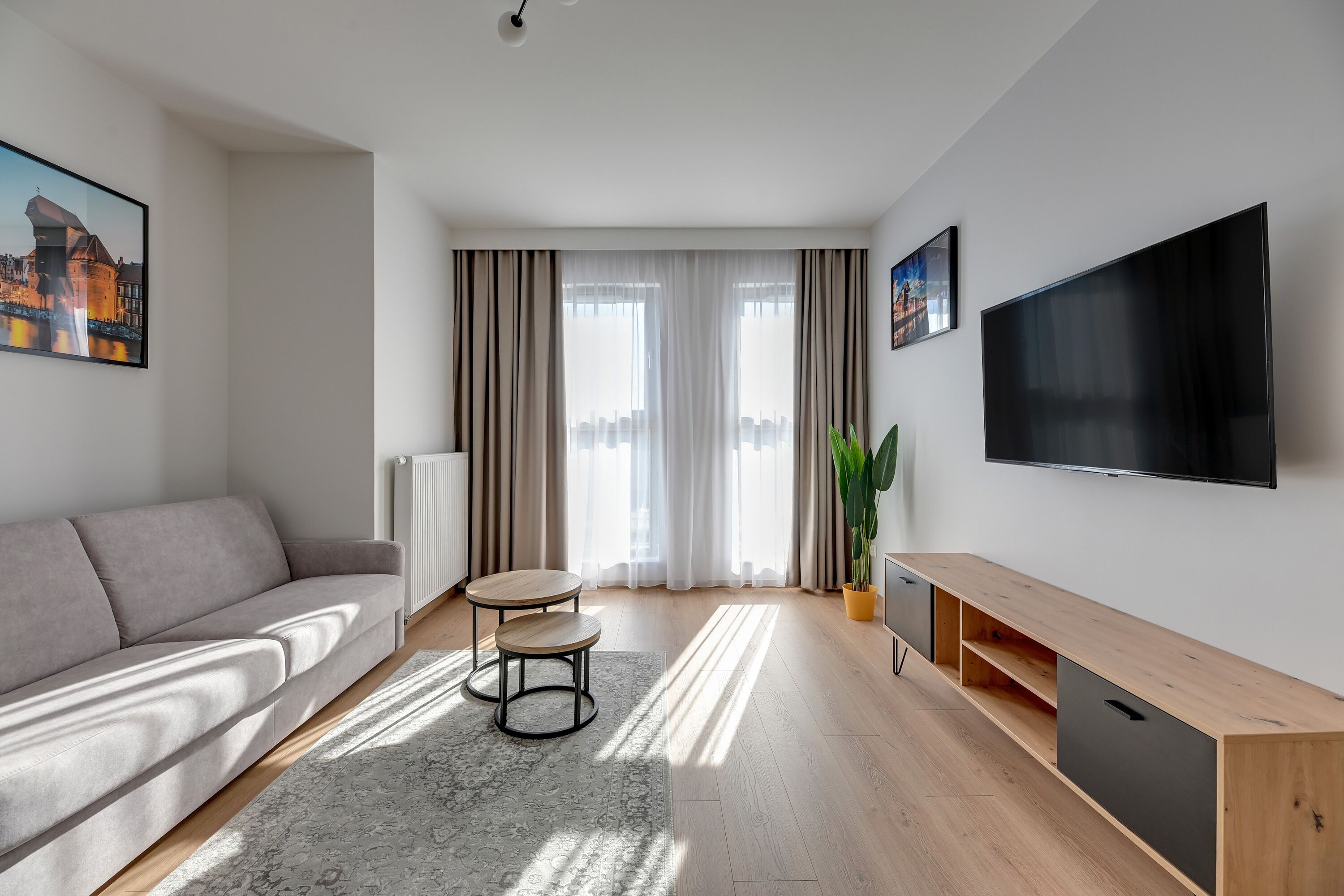 Ein modernes Wohnzimmer mit einer Couch, einem kleinen Tisch, einem Fernseher und einer Pflanze.
