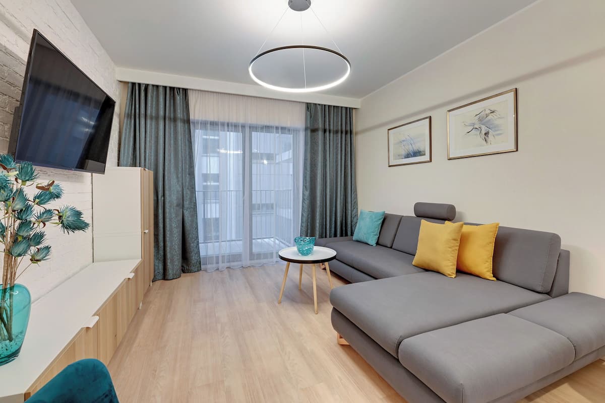 Un salon moderne avec un canapé gris, une petite table ronde et un téléviseur à écran plat fixé au mur.