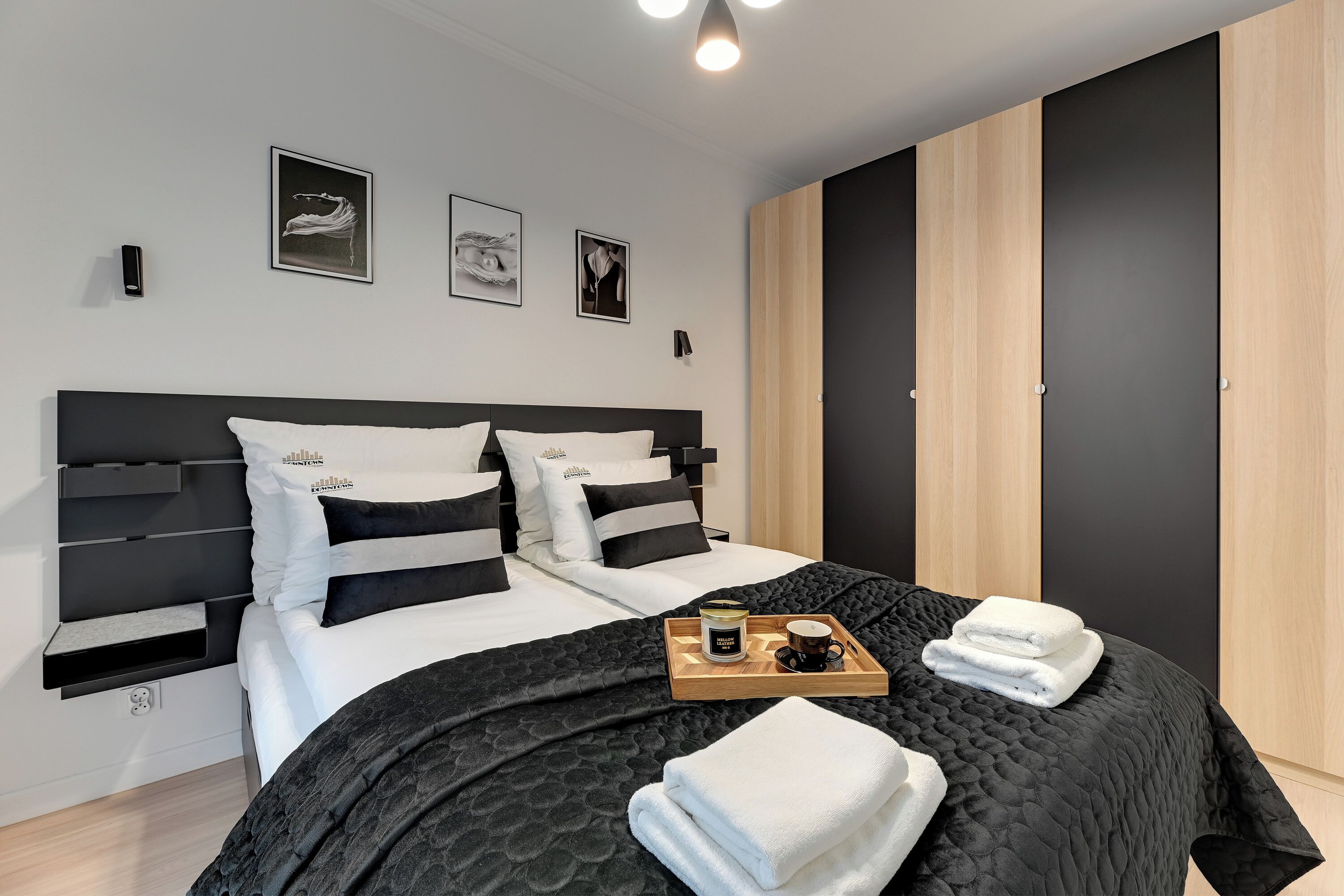 Un dormitorio moderno con colcha acolchada negra, ropa de cama blanca y una bandeja con toallas y una taza.