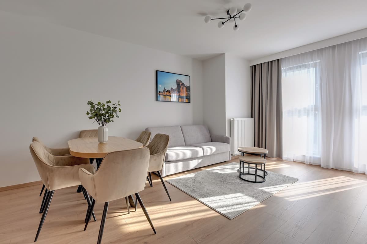 Un salon moderne avec un canapé, une table à manger et des chaises, une table basse, une plante et un tableau accroché au mur.