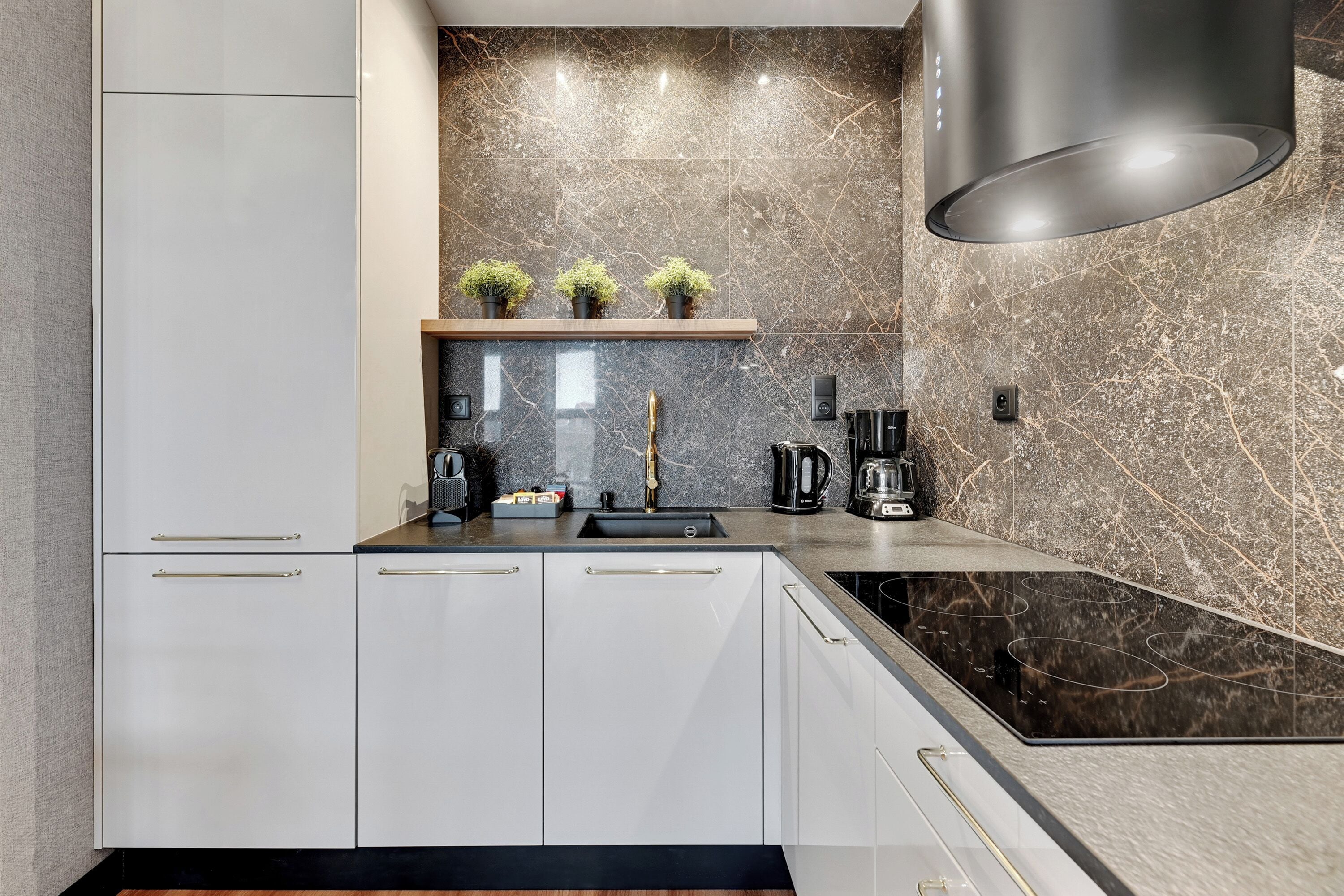 A modern kitchen with white cabinetry, a black countertop, and a marble backsplash.