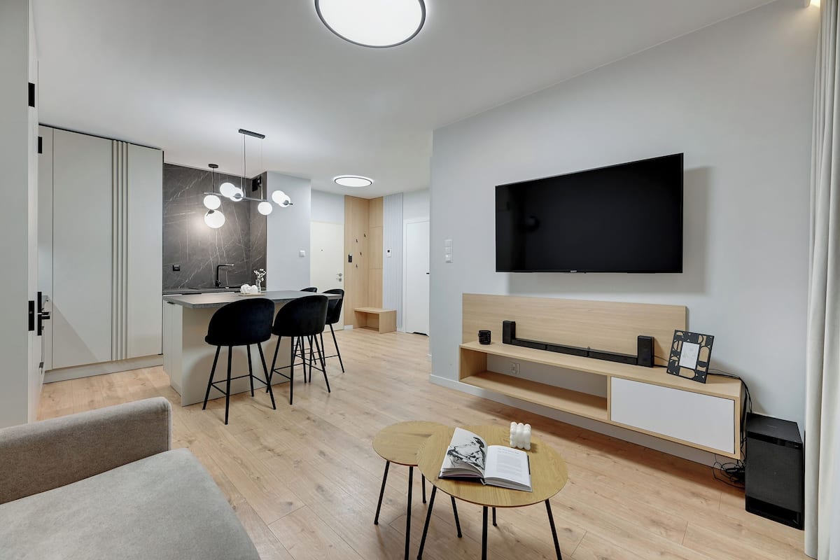 Un salon moderne doté d’un téléviseur à écran plat, d’un coin repas avec une cuisine en arrière-plan et d’un espace salon confortable.