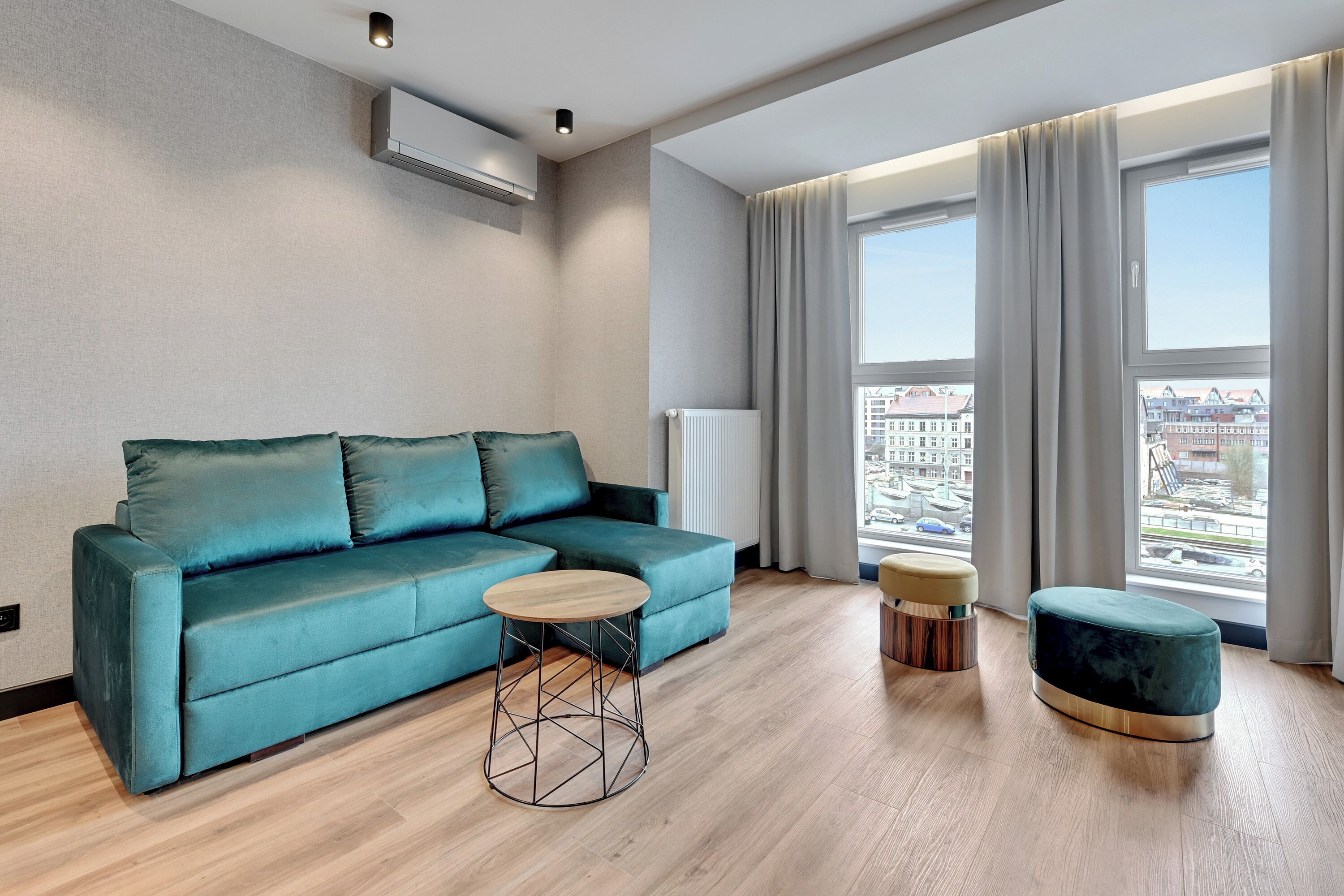 Ein modernes Wohnzimmer mit einem petrolfarbenen Sofa, einem runden Couchtisch aus Holz und einem passenden Ottomanen.