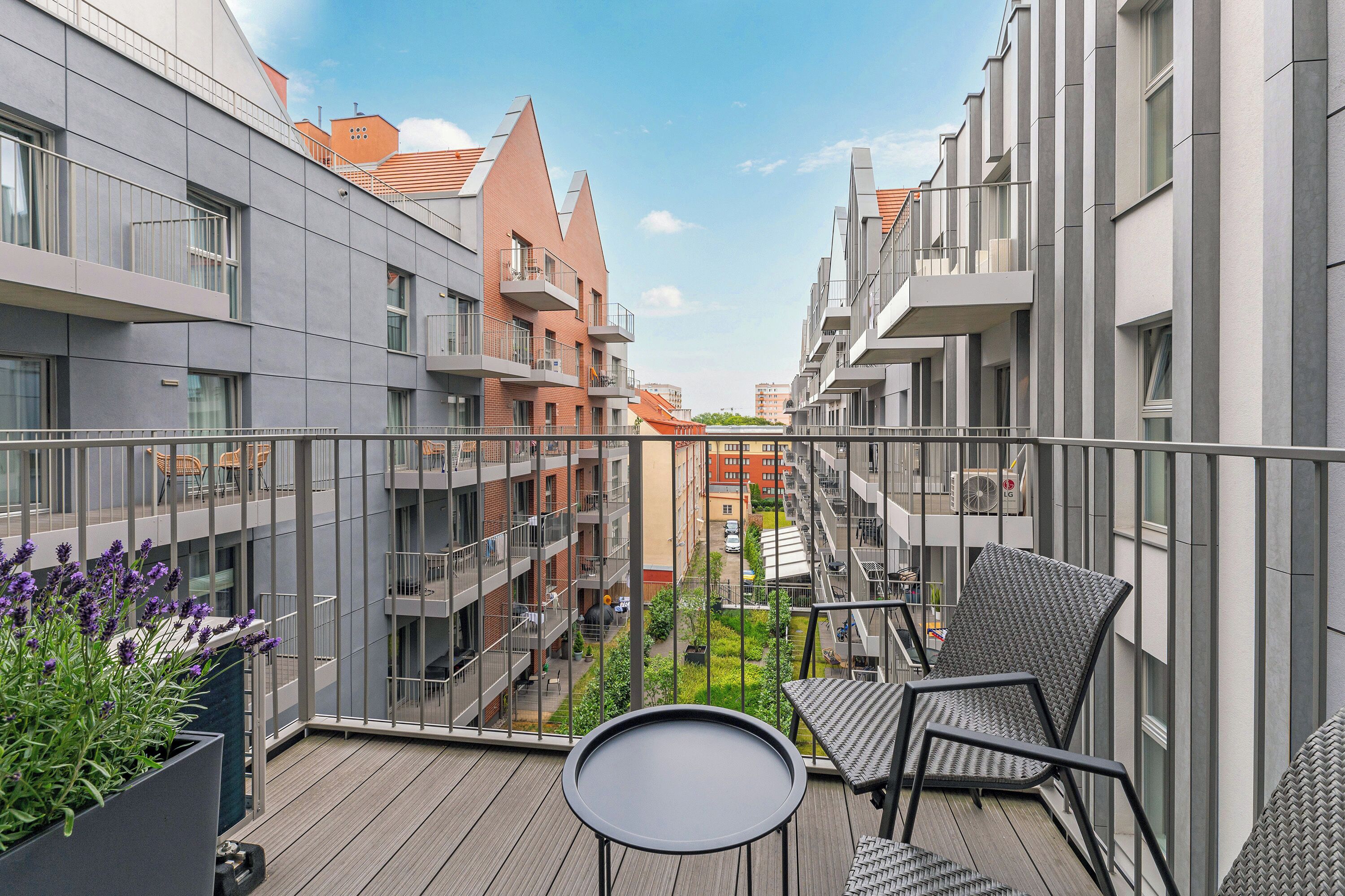 Un balcon donnant sur une cour intérieure, avec une petite table et des chaises, le tout entouré d’immeubles modernes.