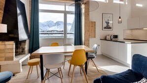 Une cuisine moderne dotée d’une cuisinière intégrée, un coin repas avec une table et des chaises en bois, et une vue sur des montagnes enneigées par de grandes fenêtres.