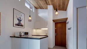Une cuisine moderne avec des meubles blancs, un îlot central, des luminaires suspendus et un plafond en bois.
