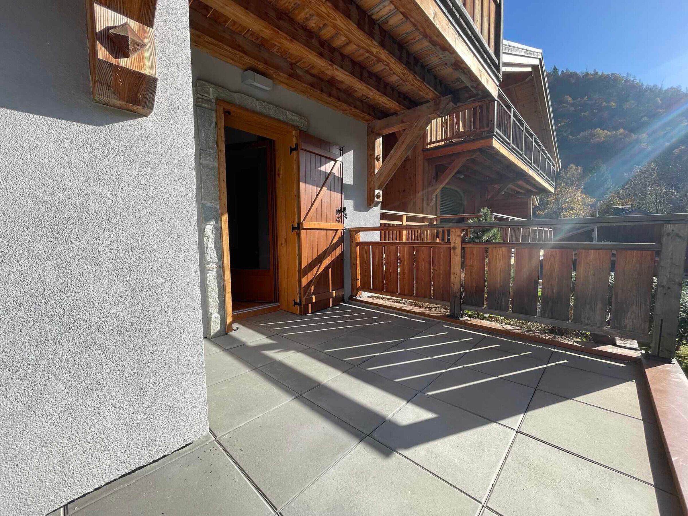 A wooden balcony with a stone wall, a wooden gate, and a view of a mountain.