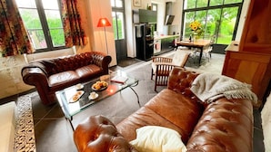 A modern living room with leather sofas, a glass coffee table, and a dining area with a table and chairs. - Charming cottage in Touraine with garden, near Loire castles (Avon-les-Roches)