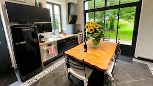 A modern kitchen with a black FrigeluX refrigerator, a built-in oven, and a large window offering a view of greenery. - Charming cottage in Touraine with garden, near Loire castles (Avon-les-Roches)