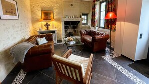 A living room with two leather sofas, a wooden chair, a fireplace, and a window with curtains. - Charming cottage in Touraine with garden, near Loire castles (Avon-les-Roches)