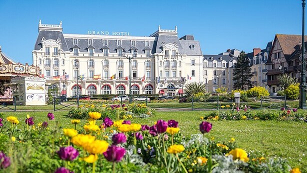 A large hotel building with the name "Grand Hotel" prominently displayed. In the foreground, there is a well-maintained garden with various flowers. - 2-room apartment, 5 people, parking, near the beach (Le Home Varaville)