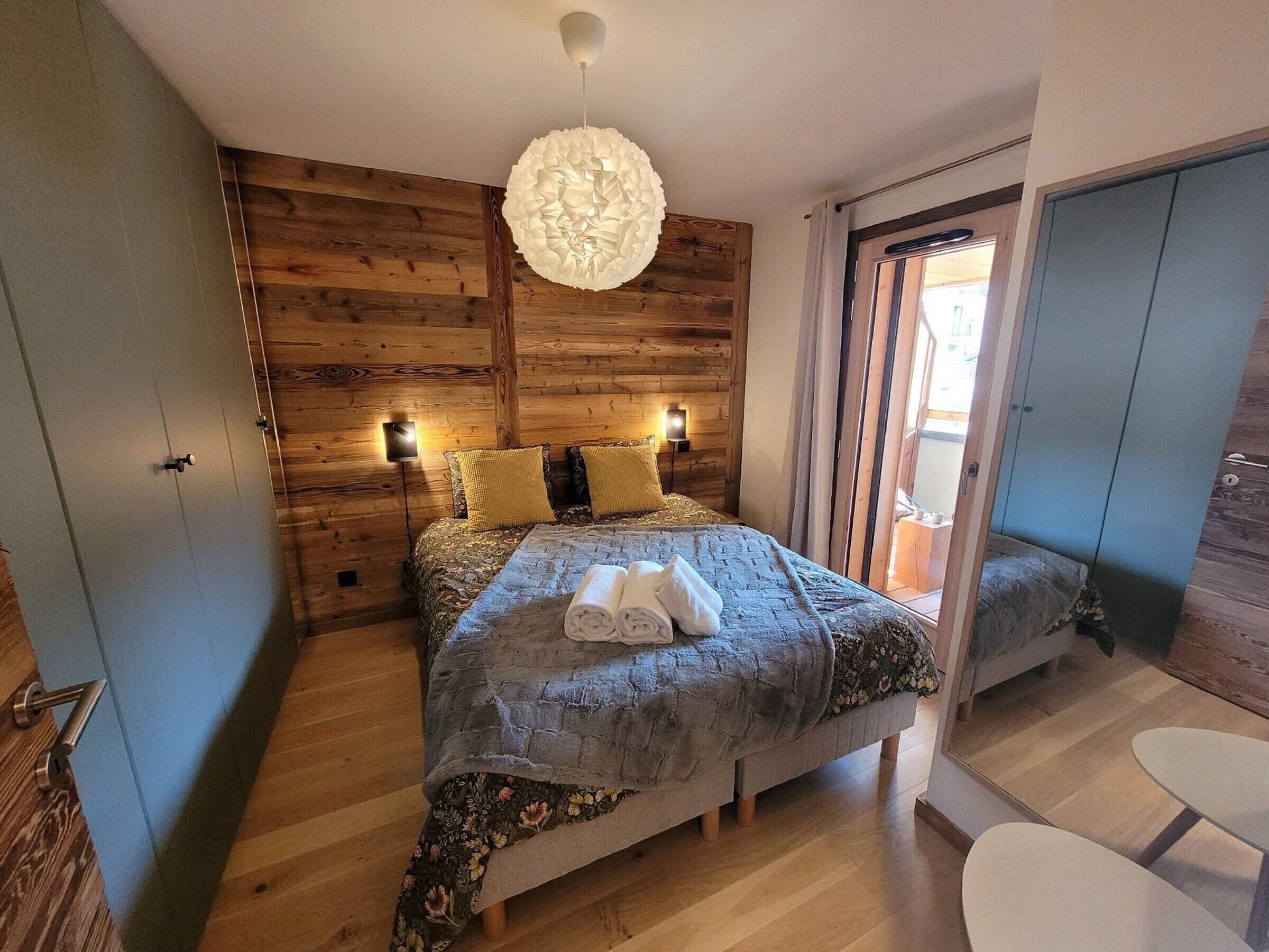 Un dormitorio con pared de madera, una cama con colcha estampada, dos lámparas de noche y una lámpara colgante.