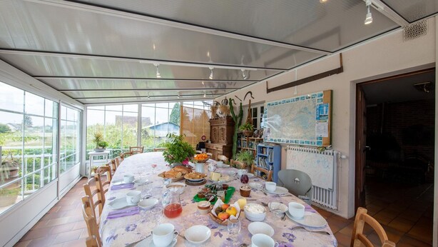 Un coin repas avec une table ronde dressée pour un repas, entourée de chaises, et offrant une vue sur la verdure à l’extérieur.