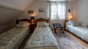 Une chambre avec deux lits simples, une table de chevet, une chaise et une fenêtre avec des rideaux.