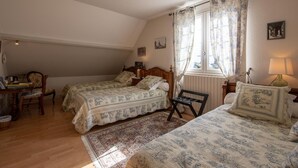 Une chambre avec deux lits, une chaise en bois, une petite table et une fenêtre avec des rideaux.